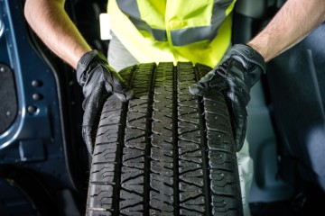 Car Tire Replacement. Tire Service. Men with Brand New Tire is Ready For Installation.