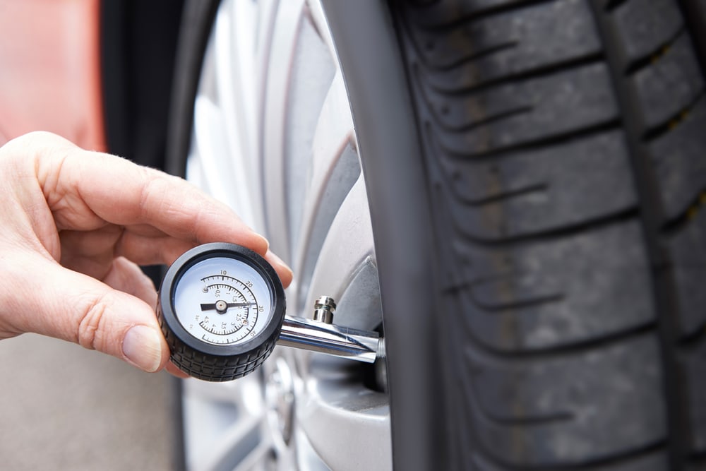 hand with tire pressure gauge on a car wheel