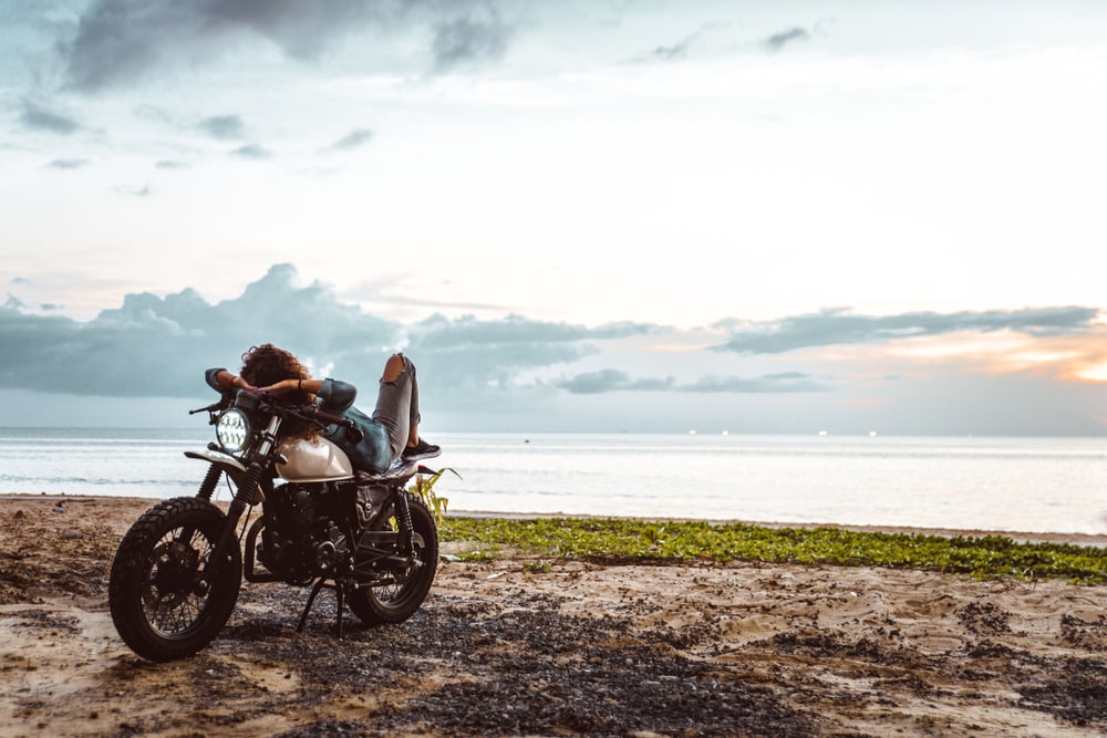 woman in motorcycle parked in front of a california beach with insurance