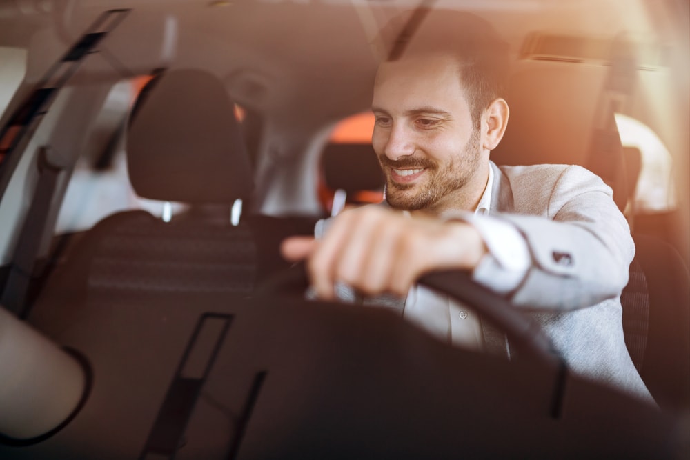 caucasian male driving car with one hand on wheel